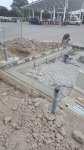 Crew finishing curved concrete curb footing at commercial gas station