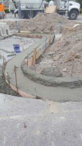 Crew finishing curved concrete curb footing at commercial gas station