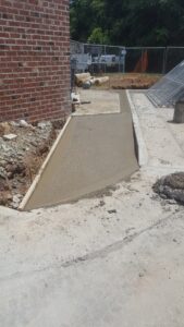 Newly poured commercial concrete walkway ramp beside brick building