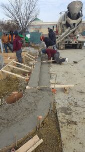 Crew screeding freshly poured curved concrete curb in wooden forms