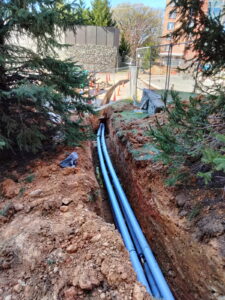 New conduit laid in an open trench with site safety fencing in place.