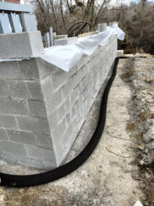 Concrete block wall under construction with drainage line in place.